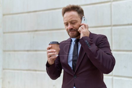 Foto de Hombre de mediana edad trabajador de negocios hablando en el teléfono inteligente beber café en la calle - Imagen libre de derechos