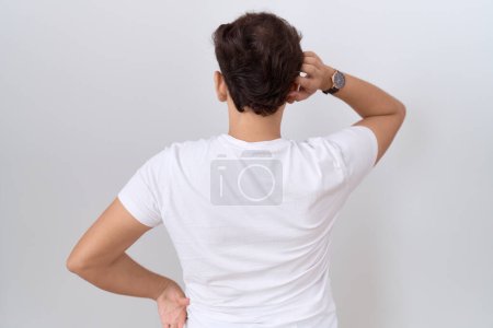 Téléchargez les photos : Jeune homme non binaire portant un t-shirt blanc décontracté à l'envers pensant au doute avec la main sur la tête - en image libre de droit