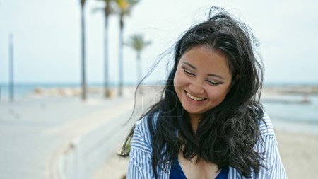 Téléchargez les photos : Jeune femme chinoise touriste souriant confiant au bord de la mer - en image libre de droit