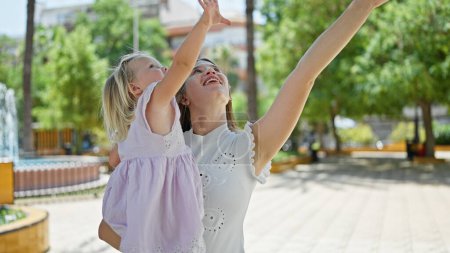 Téléchargez les photos : Mère confiante tenant sa fille joyeuse dans les bras, debout au parc, regardant vers le haut, appréciant la nature, savourant le vrai bonheur sous le ciel - en image libre de droit