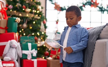 Téléchargez les photos : Africain américain garçon jouer tambourin debout par arbre de Noël à la maison - en image libre de droit