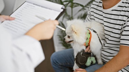Téléchargez les photos : Jeune homme caucasien anxieux patiemment assis avec son chien de compagnie bien-aimé dans la salle d'attente pour une consultation vétérinaire à la clinique vétérinaire. - en image libre de droit