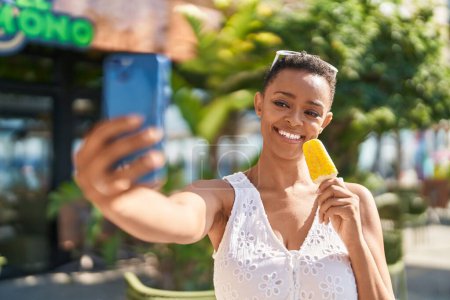 Foto de Mujer afroamericana hacer selfie por teléfono inteligente comer helado en el parque - Imagen libre de derechos