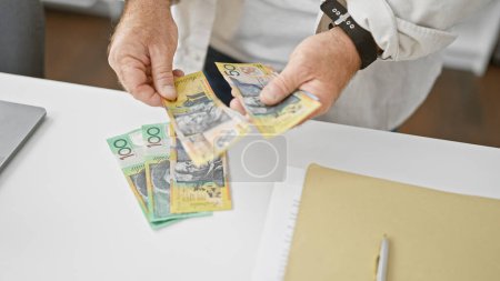 Foto de Guapo hombre de negocios caucásico de mediana edad contando montones de dólares australianos en la oficina, teniendo éxito de inversión en zancada - Imagen libre de derechos