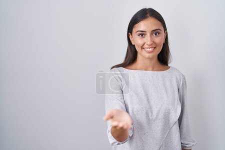 Téléchargez les photos : Young hispanic woman standing over white background smiling cheerful offering palm hand giving assistance and acceptance. - en image libre de droit