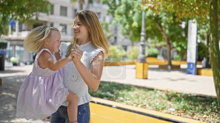 Photo for Cheerful mother dancing in the park, her smiling daughter in her arms, soaking the sunlight, basking in joy - Royalty Free Image