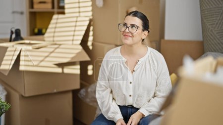 Photo for Young beautiful hispanic woman smiling looking around sitting on the sofa at new home - Royalty Free Image
