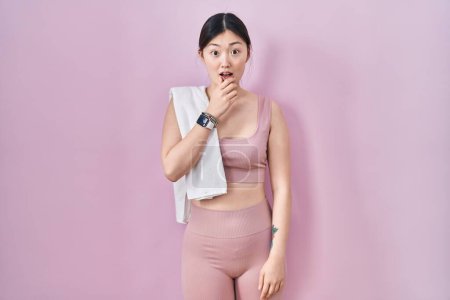 Foto de Mujer joven china con ropa deportiva y toalla que se ve fascinada con la incredulidad, sorpresa y expresión asombrada con las manos en la barbilla - Imagen libre de derechos