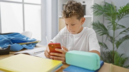 Foto de Adorable estudiante rubio, una galleta inteligente, tomando notas serias de su teléfono inteligente mientras mira su pantalla en el aula - Imagen libre de derechos