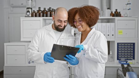 Téléchargez les photos : Deux scientifiques souriants dans le laboratoire, engloutis dans une conversation animée tout en scrutant les documents sur presse-papiers - en image libre de droit