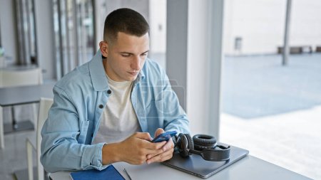 Téléchargez les photos : Beau jeune homme utilisant un smartphone à la bibliothèque universitaire moderne - en image libre de droit