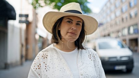 Photo for Beautiful young hispanic woman standing with serious expression looking a the camera wearing summer hat in the streets of Stockholm - Royalty Free Image