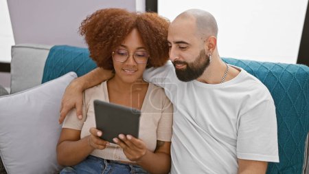 Photo for Beautiful smiling couple sitting together at home, confidently enjoying online bonding over touchpad, radiating joy in their lovely indoor living room relationship - Royalty Free Image