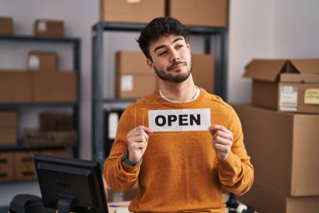 Photo for Hispanic man with beard working at small business ecommerce holding open sign smiling looking to the side and staring away thinking. - Royalty Free Image