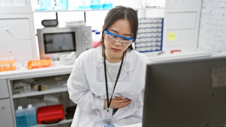 Photo for A young asian woman scientist wearing safety glasses feels stomachache in a laboratory setting - Royalty Free Image
