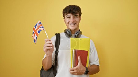 Foto de Sonriente joven adolescente hispano de pie casual, estudiante inteligente con libros, bandera del Reino Unido en la mano sobre fondo amarillo aislado, patriótico sobre su viaje de educación Inglés - Imagen libre de derechos