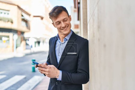 Téléchargez les photos : Jeune homme d'affaires travailleur souriant confiant en utilisant smartphone à la rue - en image libre de droit
