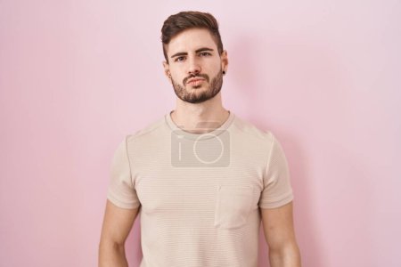 Foto de Hombre hispano con barba de pie sobre fondo rosa mirando a la cámara soplando un beso en el aire siendo encantador y sexy. expresión de amor. - Imagen libre de derechos