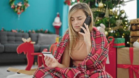 Téléchargez les photos : Jeune femme blonde faisant du shopping avec smartphone et carte de crédit célébrant Noël à la maison - en image libre de droit