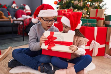 Photo for Brother and sister unpacking christmas gift sitting on floor at home - Royalty Free Image