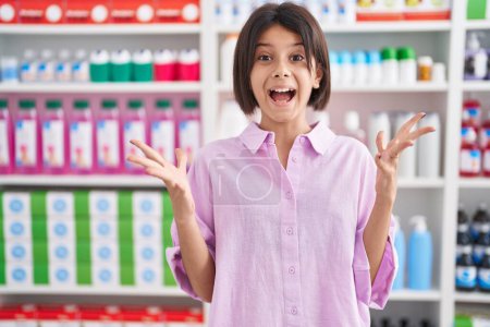 Téléchargez les photos : Jeune fille à la pharmacie pharmacie célébrant fou et étonné pour le succès avec les bras levés et les yeux ouverts hurlant excité. concept gagnant - en image libre de droit