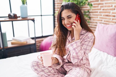 Foto de Mujer árabe hermosa joven hablando en el teléfono inteligente beber café en el dormitorio - Imagen libre de derechos