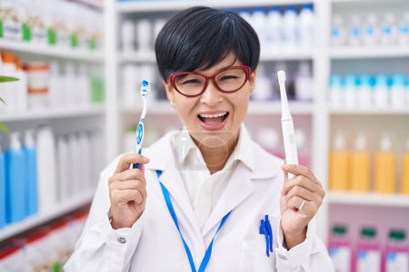 Photo for Young asian woman with short hair doing toothbrush comparative at pharmacy smiling and laughing hard out loud because funny crazy joke. - Royalty Free Image