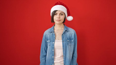 Photo for Young caucasian woman standing with serious expression wearing christmas hat over isolated red background - Royalty Free Image