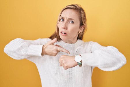 Photo for Young caucasian woman wearing white sweater over yellow background in hurry pointing to watch time, impatience, upset and angry for deadline delay - Royalty Free Image