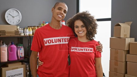 Photo for Smiling man and woman volunteers, wrapped in a warm hug at the heart of their charity center work - Royalty Free Image