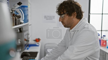 Foto de Un hombre enfocado en gafas de seguridad trabaja meticulosamente en un laboratorio moderno con equipo científico. - Imagen libre de derechos