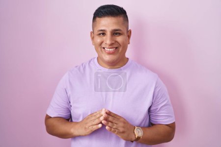 Téléchargez les photos : Jeune homme hispanique debout sur fond rose mains ensemble et doigts croisés souriant détendu et joyeux. succès et optimisme - en image libre de droit