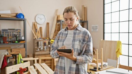 Photo for A focused young woman using a tablet in a bright, organized carpentry workshop. - Royalty Free Image