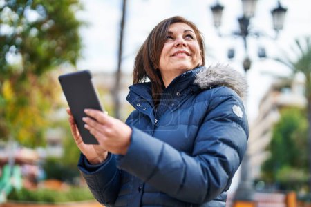 Téléchargez les photos : Femme d'âge moyen souriant confiant en utilisant le pavé tactile au parc - en image libre de droit