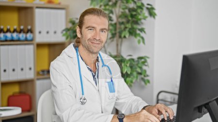 Photo for A confident male doctor with a stethoscope works in a hospital office, symbolizing healthcare professionalism indoors. - Royalty Free Image