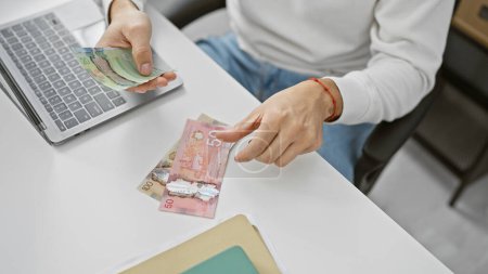 Téléchargez les photos : Homme comptant les dollars canadiens à un bureau moderne, mettant en valeur la monnaie et le milieu de travail. - en image libre de droit