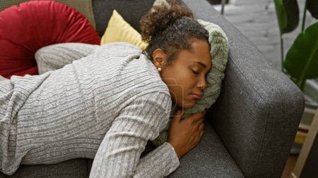 Foto de Una joven con el pelo rizado duerme tranquilamente en un sofá rodeado de cojines en una acogedora sala de estar. - Imagen libre de derechos
