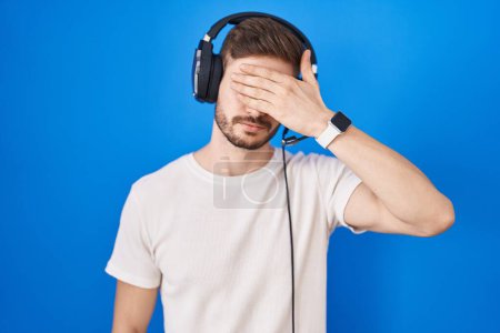 Photo for Hispanic man with beard listening to music wearing headphones covering eyes with hand, looking serious and sad. sightless, hiding and rejection concept - Royalty Free Image