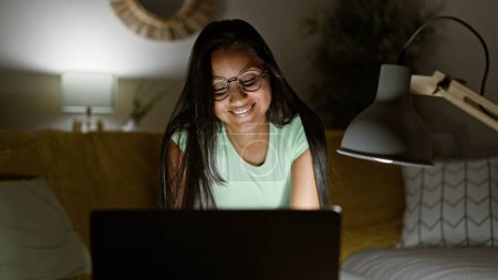 Téléchargez les photos : Jeune femme latine utilisant un ordinateur portable portant des lunettes souriant à la maison - en image libre de droit