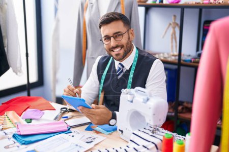 Photo for Young hispanic man tailor smiling confident drawing on touchpad at tailor shop - Royalty Free Image