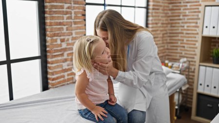 Photo for Pediatrician doctor at clinic examining ear, serious expression as child patient stands indoors - Royalty Free Image