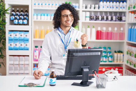 Photo for Hispanic man with curly hair working at pharmacy drugstore very happy and excited doing winner gesture with arms raised, smiling and screaming for success. celebration concept. - Royalty Free Image