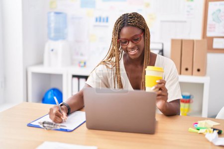 Téléchargez les photos : Femme afro-américaine travailleur d'affaires en utilisant l'écriture d'ordinateur portable sur le document au bureau - en image libre de droit