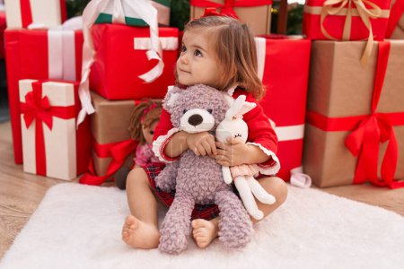 Photo for Adorable blonde toddler holding teddy bear sitting on floor by christmas gifts at home - Royalty Free Image