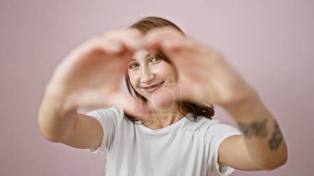 Foto de Mujer joven sonriendo confiado haciendo gesto del corazón con las manos sobre el fondo rosa aislado - Imagen libre de derechos