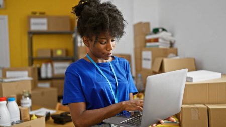 Téléchargez les photos : Femme afro-américaine bénévole utilisant un ordinateur portable au centre de charité - en image libre de droit