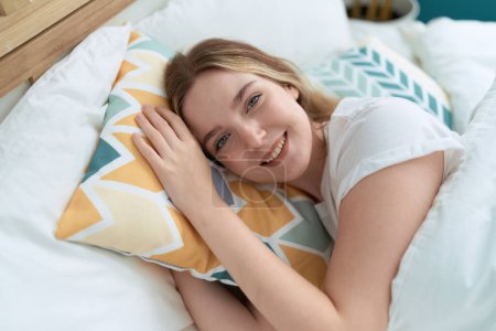 Foto de Joven mujer caucásica sonriendo confiada acostada en la cama en el dormitorio - Imagen libre de derechos
