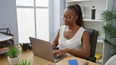 Photo for An african american woman working attentively on a laptop in a modern office setting. - Royalty Free Image