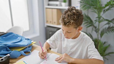 Foto de Adorable estudiante rubio que se concentra y toma notas en su escritorio en el aula - Imagen libre de derechos
