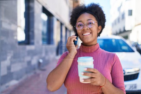 Foto de Mujer afroamericana hablando en smartphone bebiendo café en la calle - Imagen libre de derechos